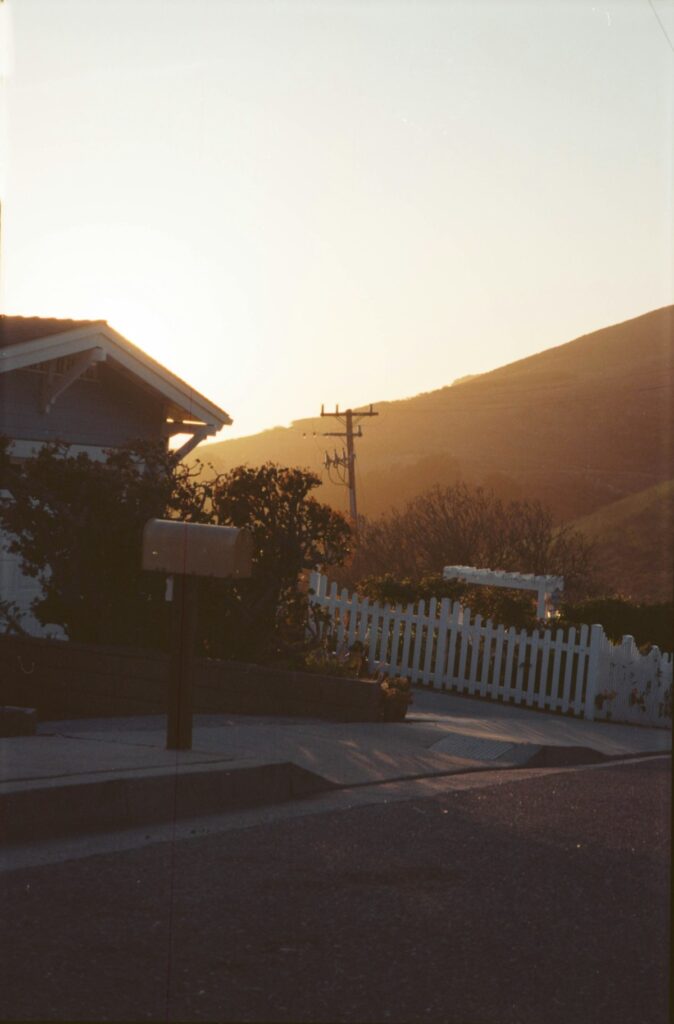 A quiet residential street with a white fence and dry hills rising behind the houses